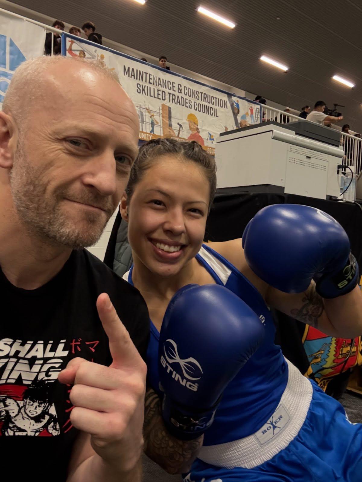 A coach and smiling boxer in blue gloves beside the ring